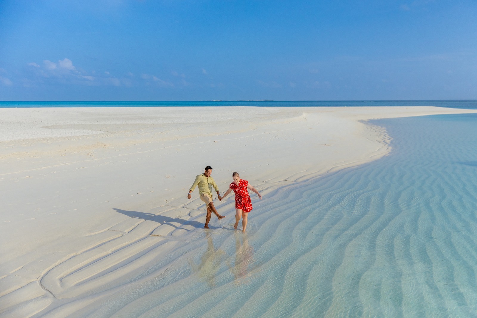 Nadine and Sobah walking hand-in-hand along a pristine white sandbar